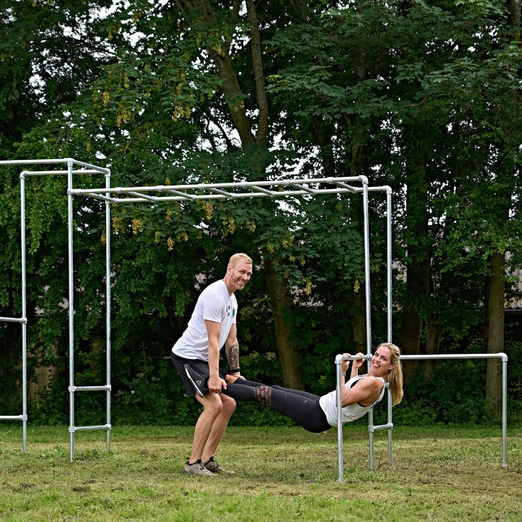 Kvinde og mand træner sammen på crossfit stativ i haven