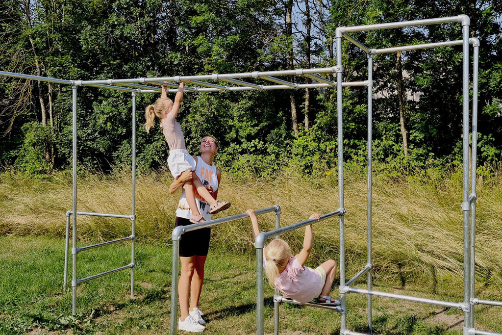 Mor træner og leger med sine små piger på klatrestativet i haven