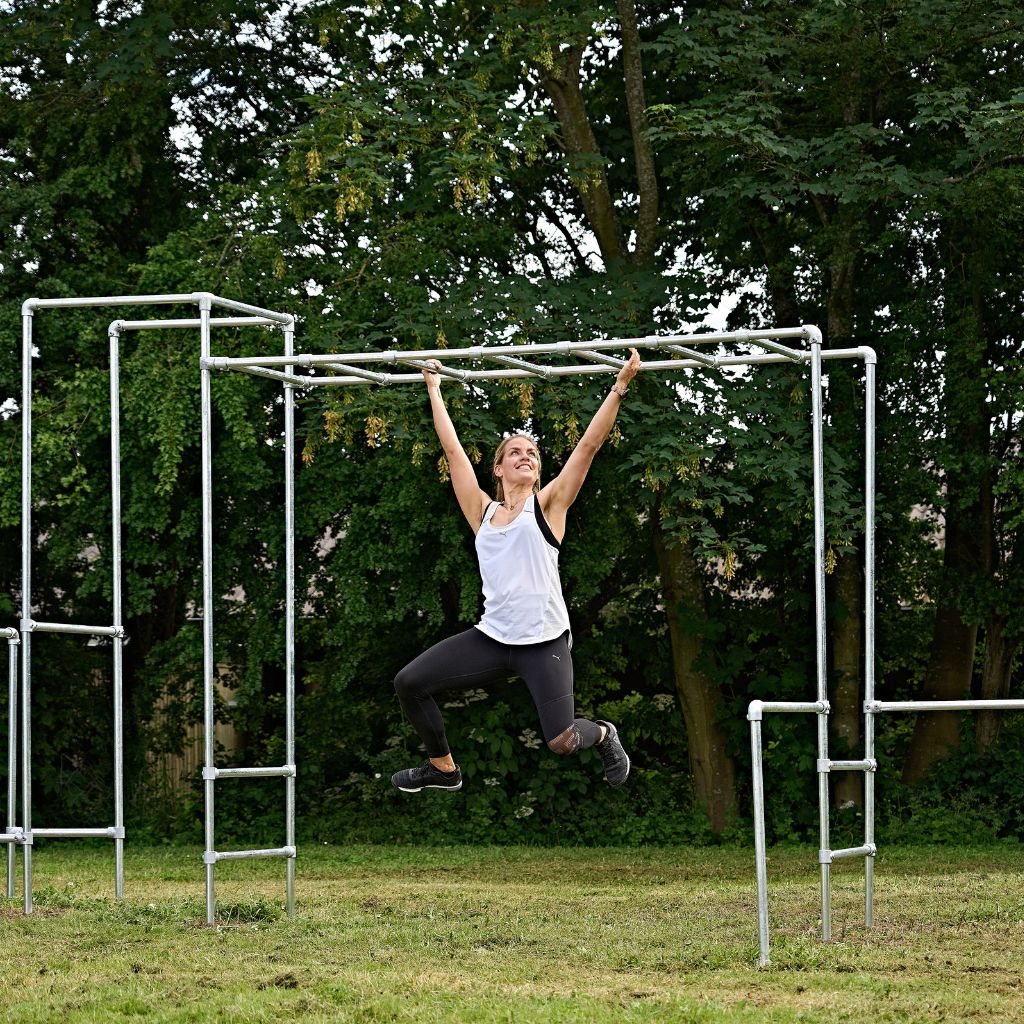 Kvinde styrketræner med sidelæns armgang på træningsstativ i haven